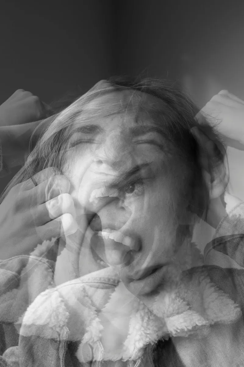 Black and white multiple-exposure photograph of a person with hands on their face, showing motion blur that conveys inner turmoil