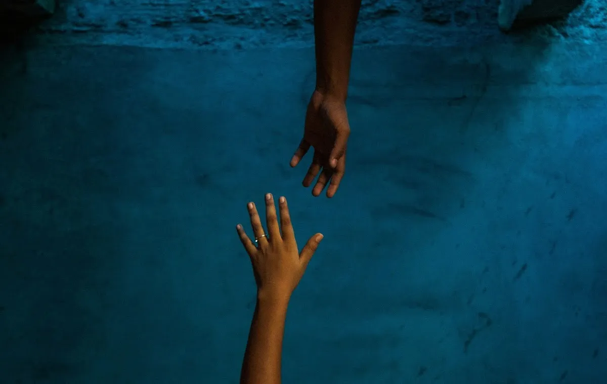 Two hands reaching toward each other in dim blue light — a gesture of help and connection